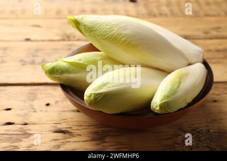 Fresh raw Belgian endives (chicory) in bowl on wooden table Stock Photo