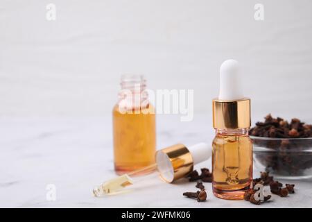 Aromatic clove oil in bottles and dried buds on white table, closeup. Space for text Stock Photo