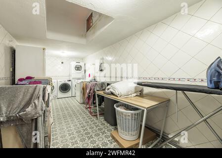 A room dedicated to laundry on the ground floor of a house full of clotheslines full of clothes, washing machines, dryers and ironing utensils Stock Photo