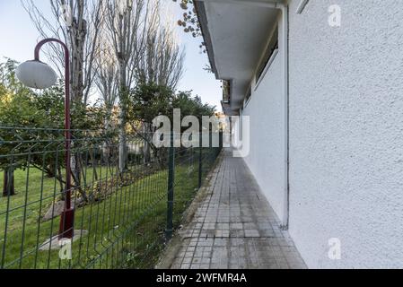 Exterior perimeter corridor with metal fence around a residential building with landscaped common areas with grass and manicured hedges Stock Photo