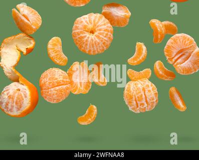 Flying sweet peeled mandarins on green background Stock Photo