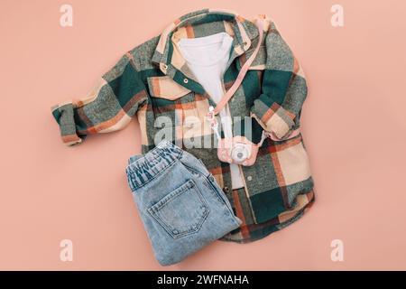 Children's checkered shirt and blue jeans with digital camera on pink background Stock Photo