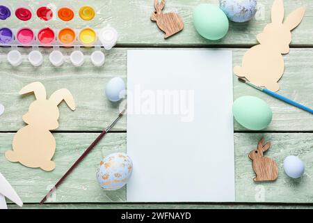 Blank card with rabbits, paints and Easter eggs on color wooden background Stock Photo