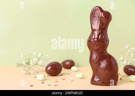 Chocolate Easter bunny with eggs and flowers on table against green background Stock Photo