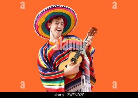 Portrait of young Mexican man in sombrero and poncho playing guitar on orange background Stock Photo