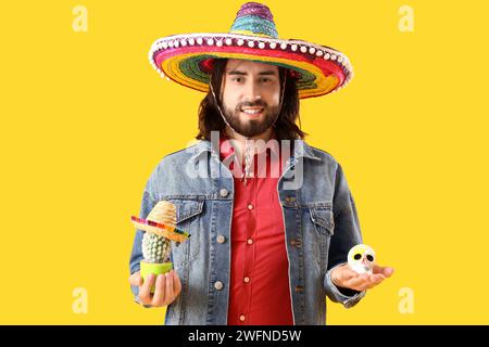 Handsome young Mexican man with cactus and painted skull on yellow background. Celebration of Day of the Dead Stock Photo