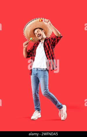 Happy young Mexican man in sombrero and with maracas on red background Stock Photo