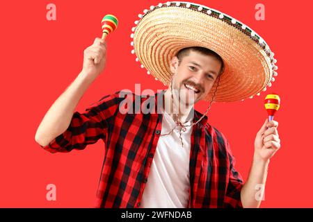 Happy young Mexican man in sombrero and with maracas on red background Stock Photo