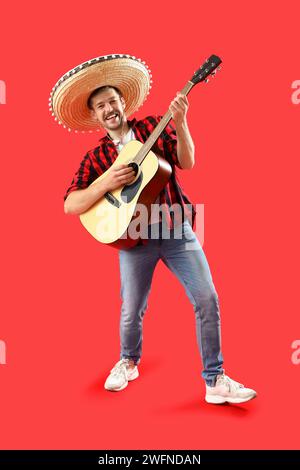 Young man in sombrero playing guitar on red background Stock Photo