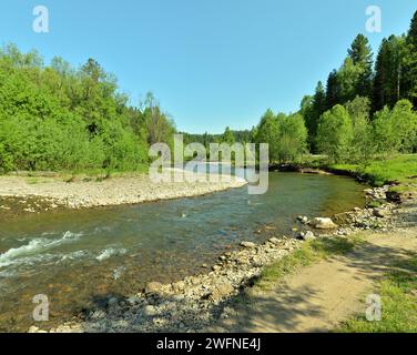 A shallow, turbulent river with a rocky bottom and banks calmly flows ...