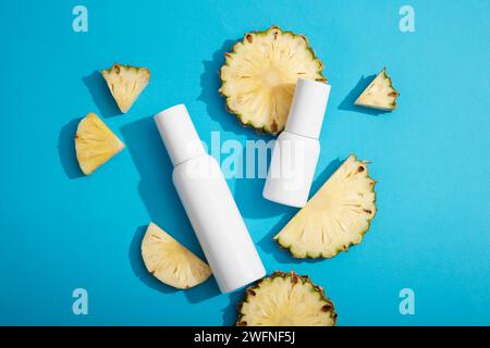 Against a blue background, some pineapple slices and white empty label bottles are displayed. Product presentation. pineapple (Ananas comosus) used to Stock Photo