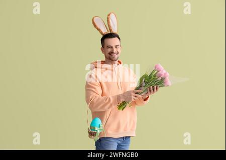 Young man in bunny ears with tulips and Easter egg on green background Stock Photo