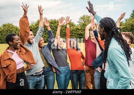 A vibrant group of friends cheerfully raise their hands in celebration, enjoying a lively moment in the park. Stock Photo