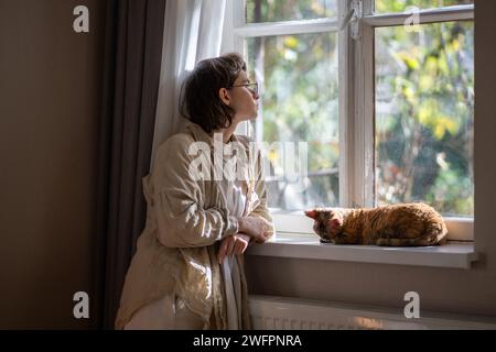 Melancholic pet owner looking at window in depression while staying at home in sunny summer day Stock Photo
