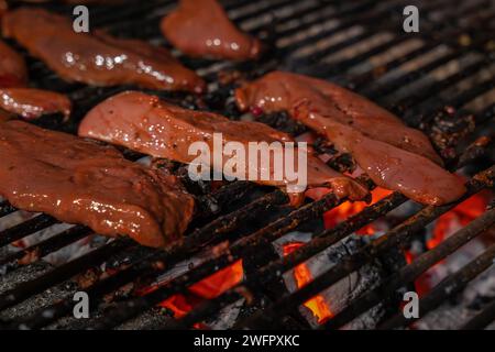 Lamb liver on the grill. A close-up of burning barbecue coals and lamb liver slices. Stock Photo