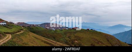 Panoramic view of highland road, houses and mountains. Autumn colors on the trees. Cold snowy mountains. Stock Photo