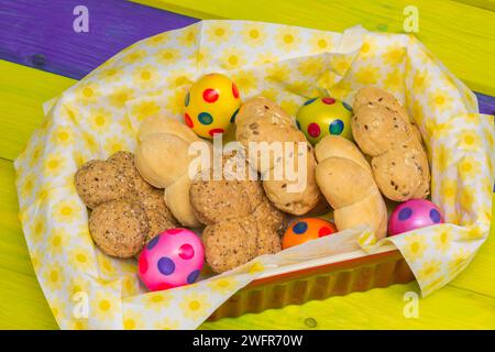 Bread rolls and colorful easter eggs in a basket on a yellow wooden table Stock Photo