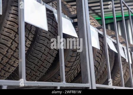 Close-up image of new car tires arranged on metal shelving in outdoors shop. Clean information plates for information placement. Stock Photo