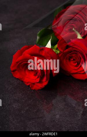 Set of three red roses in a bouquet laying on a dark grey textured surface. Vertical image Stock Photo
