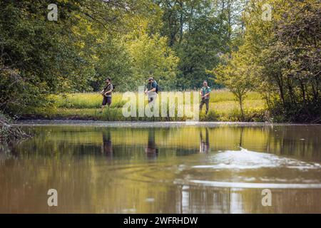 Three anglers enjoying fishing surrounded by the lush green nature of the river shore. Outdoor hobby and activity concept. Stock Photo