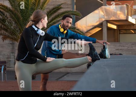Young smiling couple with sports headphones doing stretching. Stock Photo
