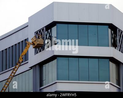 Cairo, Egypt, January 25 2024: Painting service and maintenance of the exterior of a building, the worker is on a hydraulic bucket boom lift vehicle, Stock Photo