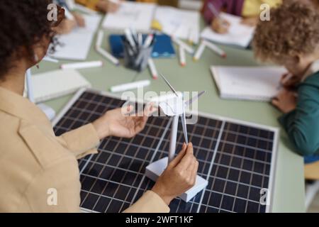 Close up of young teacher holding wind turbine model while explaining renewable energy to group of children in school copy space Stock Photo