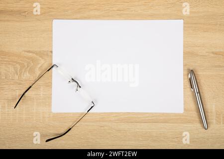 Modern Minimalist Workspace: White Paper, Reading Glasses, and Silver Marker on Wooden Desk. Stock Photo