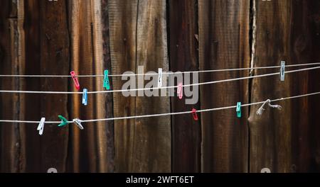 Colorful clothespins hanging on washing line or rope against the background of a wooden fence. Banner. Selective focus. Stock Photo