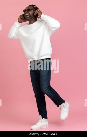 Excited black man wearing white sweatshirt listening music in headphones black man wearing white sweatshirt Stock Photo