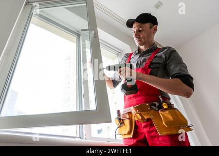 Professional installer of plastic windows poses in a working uniform, holds glasses with his hand. Specialist in the installation of plastic windows Stock Photo