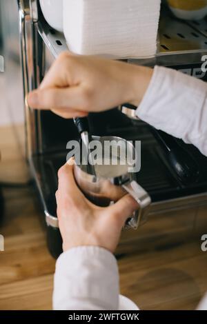 A barista prepares milk for cappuccino using an espresso machine. Close-up of a man preparing coffee in a cafe. Stock Photo
