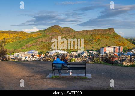 Lonely couple on a bench on the Calton Hill with view to Holyrood Park with Arthur's Seat at sunset in city of Edinburgh, Scotland, UK. Stock Photo