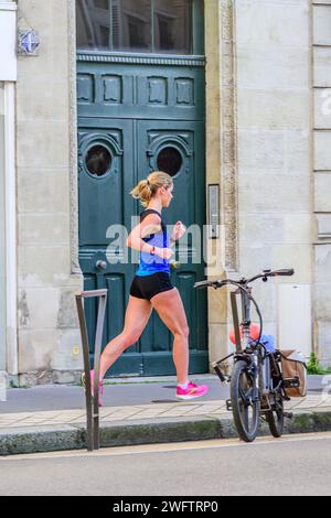 Fit young woman in sports clothing running along city pavement - Tours, Indre-et-Loire (37), France. Stock Photo