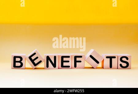 Benefits word on wooden blocks on a beautiful yellow background. Copy space Stock Photo