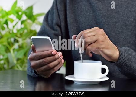 Closeup shot of a young man using a cellphone and drinking a coffee while sitting in a cafe Stock Photo