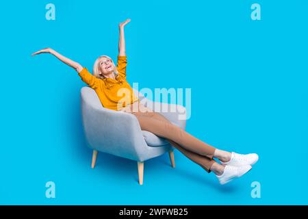 Full length photo of lovely senior lady armchair look up empty space dressed stylish yellow satin garment isolated on blue color background Stock Photo