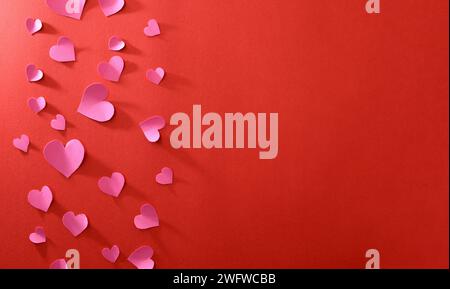 Love background with fuxia pink heart cutouts of various sizes on the left edge isolated on a red background. Top view. Stock Photo
