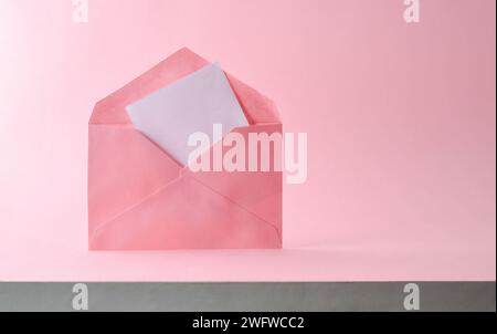 Open pink envelope with empty white sheet with heart cutouts coming out on pink textured background. Top view. Stock Photo