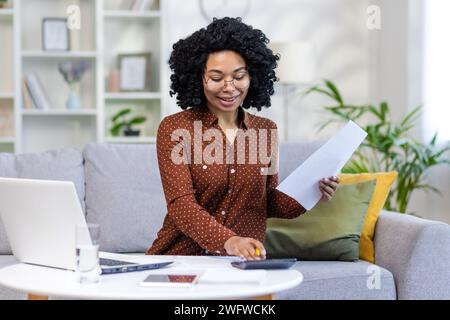 Remote work at home. African American woman doing paperwork and accounts at home, checking data, using calculator. Stock Photo