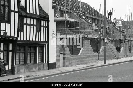 1987, a new brick building being constructed beside a 15th century, half-timbered tavern, The Black Swan Inn, Peasholme Green, Helmsley, York, England, UK. The old inn or tavern was orginally built as a home for the Bowes Family. The new building next to ot, the Peasholme Centre, was built as a hostel for local homeless people. This modern building had a much shorter life, being demolished in 2010. Stock Photo
