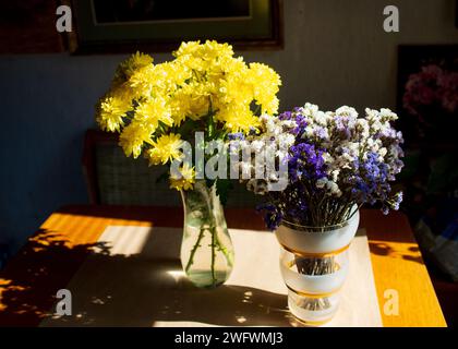 A transparent glass vase with bright yellow chrysanthemums stands next to a bouquet of natural dried flowers. Stock Photo