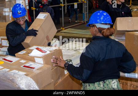 YOKOSUKA, Japan (Jan. 9, 2024) Logistics Specialist 3rd Class Tanasha Smith, from Columbus, Ohio, left, and Logistics Specialist 2nd Class Davena Campbell, from Clarendon, Jamaica, move boxes while sorting supply orders in the hangar bay of the U.S. Navy’s only forward-deployed aircraft carrier, USS Ronald Reagan (CVN 76), while in-port Commander, Fleet Activities Yokosuka, Jan. 9. Ronald Reagan, the flagship of the Carrier Strike Group 5, provides a combat-ready force that protects and defends the United States, and supports alliances, partnerships and collective maritime interests in the Ind Stock Photo