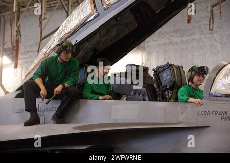 Sailors assigned to the 'Blacklions' of Strike Fighter Squadron (VFA) 213 perform maintenance on an F/A-18F Super Hornet in the hangar bay of the world's largest aircraft carrier, Jan. 6, 2024. The U.S. maintains forward-deployed, ready, and postured forces to deter aggression and support security and stability around the world. Stock Photo