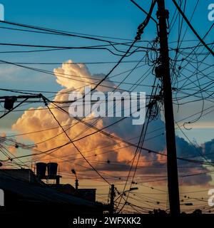 A beautiful large cloud imprisoned by the meshes of a tangle of electrical cables at sunset. Armenia, Quindío, Colombia. Stock Photo