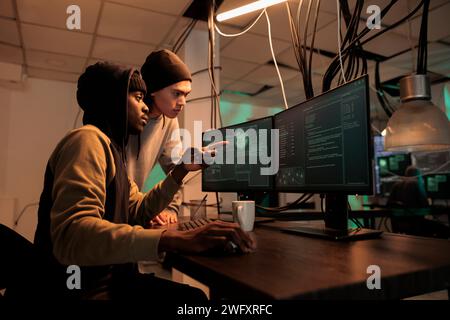 Diverse hackers planning data breach with virus, analyzing firewall encryption to hack computer system. Young team of spies working on breaking database server, steal passwords. Stock Photo