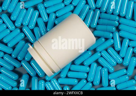 Blue antibiotic capsule pills texture with white bottle. Pharmaceutical production. Global health. Resistance to antibiotic drugs. Gelatin capsule pil Stock Photo