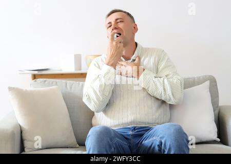 Ill mature man using spray for sore throat at home Stock Photo