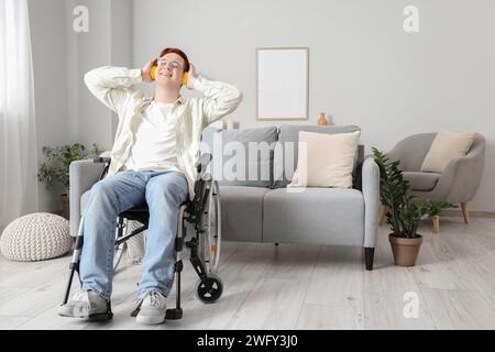 Young man in wheelchair with headphones listening to music at home Stock Photo