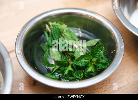 A close-up of vibrant fresh mint leaves soaking in water in a stainless steel bowl on a wooden surface. Stock Photo